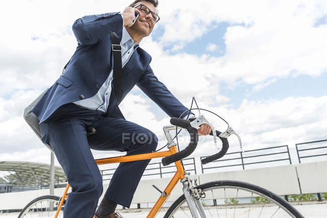 Empresario en bicicleta, hablando por teléfono - foto de stock