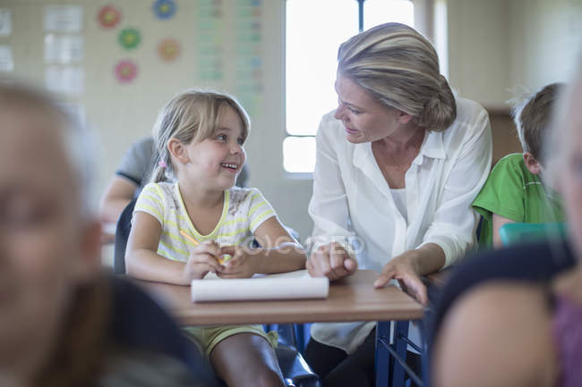 Smiling teacher talking to schoolgirl in classroom — Stock Photo