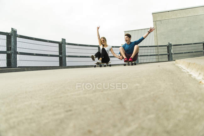 Entusiástico jovem casal cavalgando colina abaixo com skates — Fotografia de Stock
