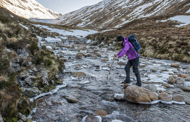 Reino Unido, Escocia, Ben Nevis, Carn Mor Dearg, mountaineer crossing river - foto de stock