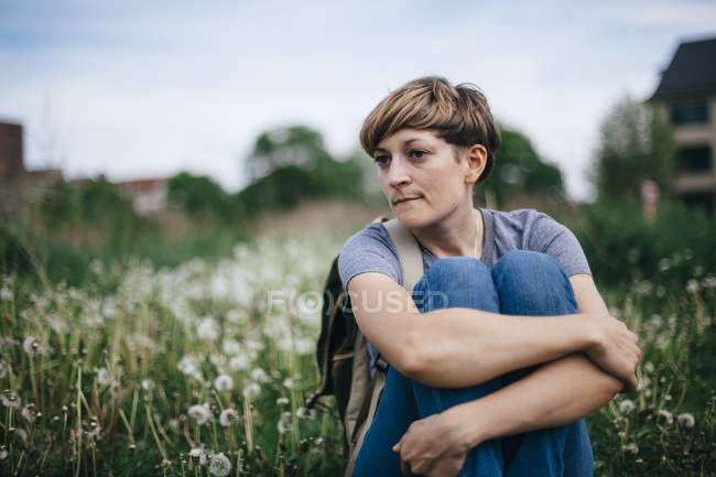 Retrato de uma jovem sentada em um prado abraçando joelhos — Fotografia de Stock