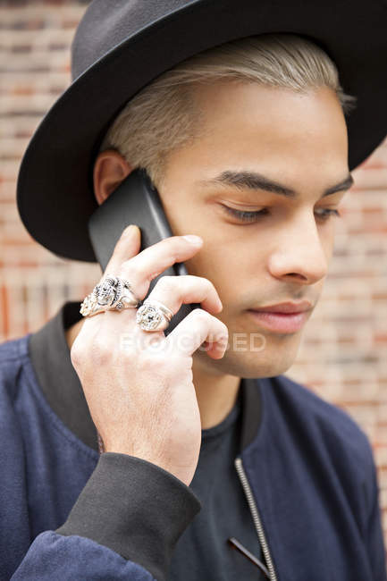 Портрет молодого человека в кольцах и шляпе, звонящего со смартфона — стоковое фото