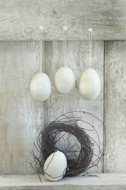 Œufs de Pâques et nid devant une étagère en bois — Photo de stock