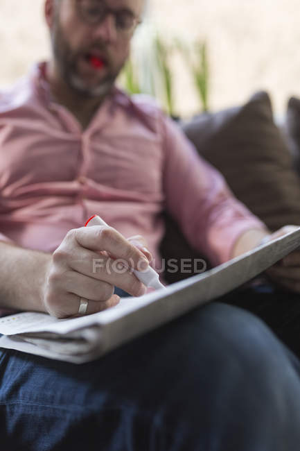 Mature man sitting on couch marking advertisments in newspaper — Stock Photo