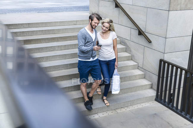 Germany, Cologne, young couple looking at smartphone walking downstairs — Stock Photo