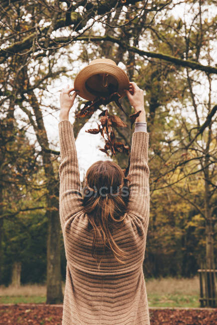 Mujer dejando caer las hojas en la cabeza del sombrero - foto de stock