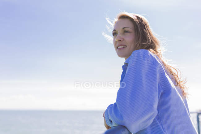 Sorrindo mulher pensativa em pé à beira-mar — Fotografia de Stock
