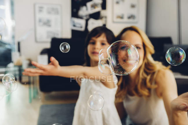 Felice madre con figlia a casa soffiando bolle di sapone — Foto stock