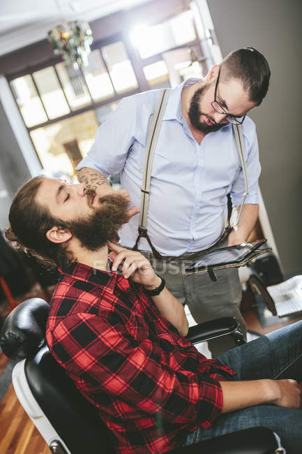 Barbier avec client utilisant une tablette numérique dans le salon de coiffure — Photo de stock
