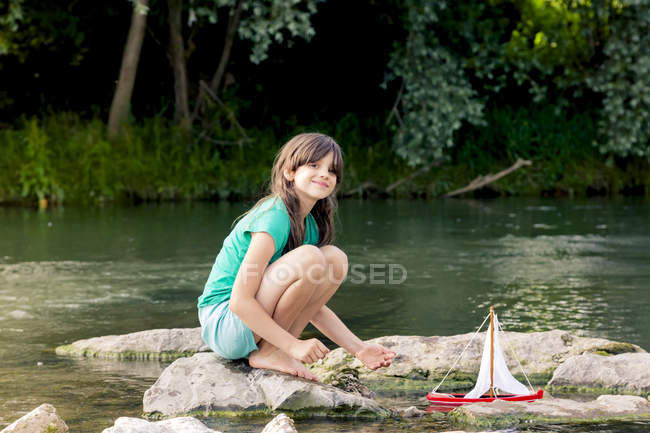 Girl playing with wooden toy boat at a river — Stock Photo