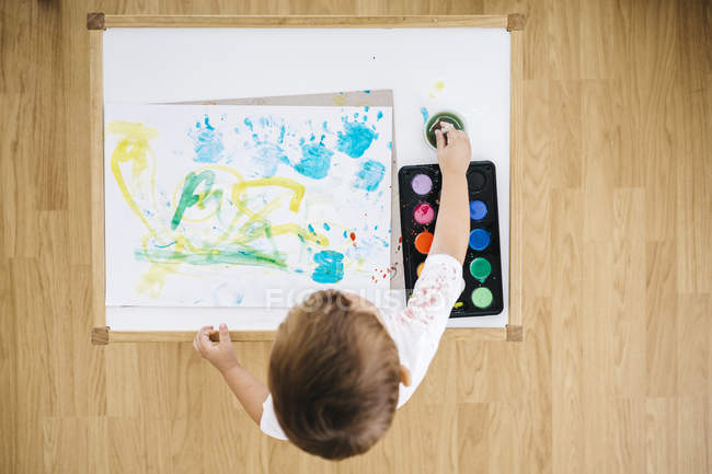 Pequeño niño pintando con acuarelas en suelo de madera - foto de stock