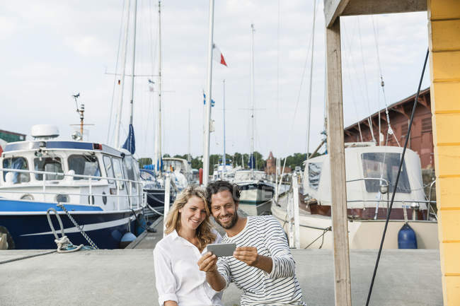 Germany, Luebeck, smiling couple at marina with smartphone — Stock Photo
