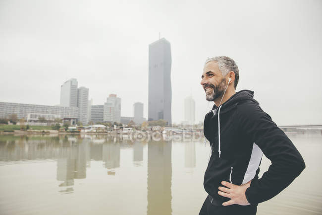 Österreich, Wien, Porträt einer lächelnden Joggerin mit Kopfhörern vor der Stadt Donau — Stockfoto