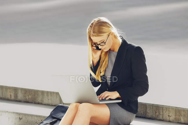 Femme d'affaires assis sur les marches à l'aide d'un ordinateur portable et téléphone portable — Photo de stock