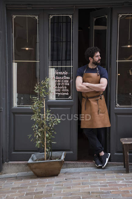 Craftsman with leather apron and arms crossed standing at the entrance of his workshop — Stock Photo