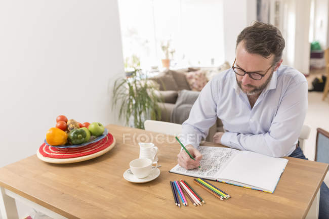 Uomo seduto al tavolo di legno con libro da colorare e matite colorate — Foto stock