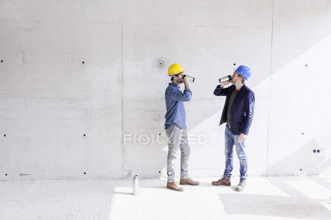 Dos hombres en construcción bebiendo de tazas - foto de stock