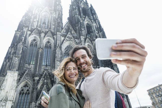 Germany, Cologne, portrait of young couple taking a selfie in front of Cologne Cathedral — Stock Photo