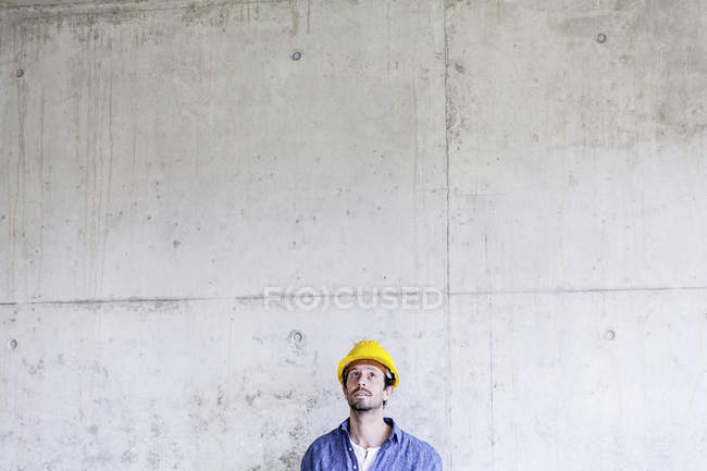 Uomo con cappello rigido in cantiere al muro di cemento guardando in alto — Foto stock
