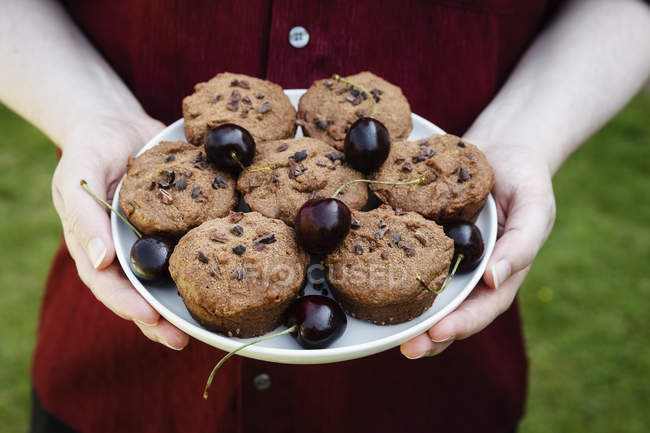 Vista ritagliata di persona in possesso di piatto con muffin al cioccolato vegan e ciliegie — Foto stock