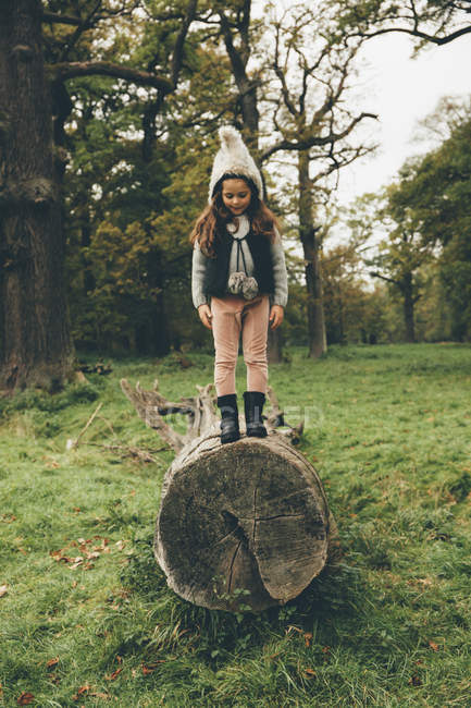 Little girl wearing cap standing on a tree trunk in autumnal park — Stock Photo