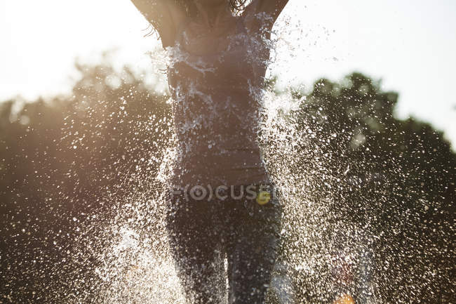 Woman running through fountain splashing water drops — Stock Photo