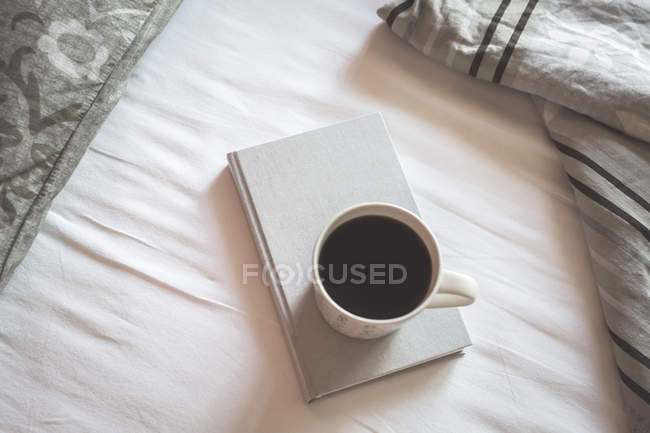 Книга и чашка черного кофе на кровати — стоковое фото