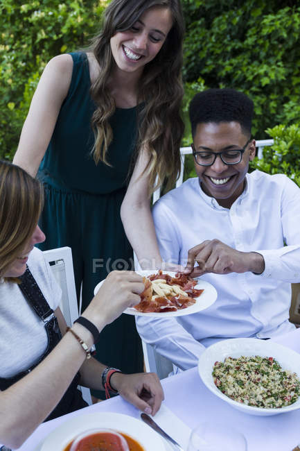Femme offrant jambon espagnol à ses invités lors d'un dîner d'été — Photo de stock