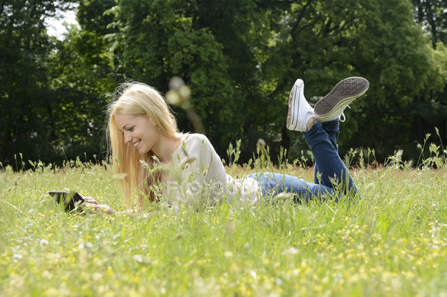 Jovem deitada em um prado usando tablet digital — Fotografia de Stock
