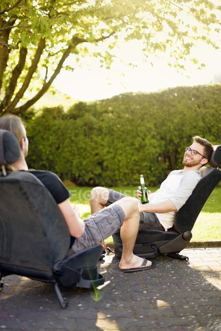 Two young men sitting on removed car seats drinking beer — Stock Photo