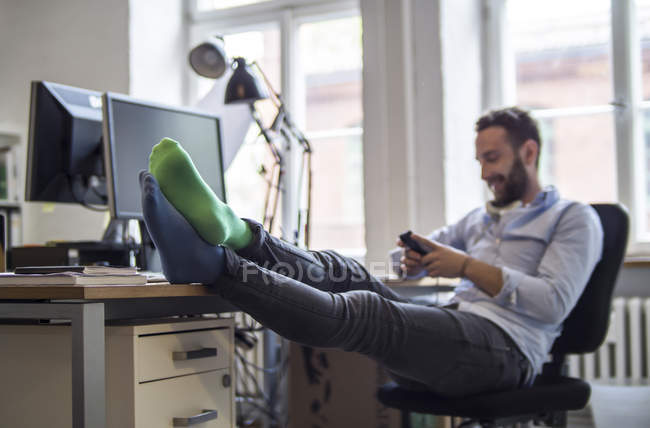 Jeune homme au bureau avec les pieds sur le bureau portant des chaussettes différentes — Photo de stock