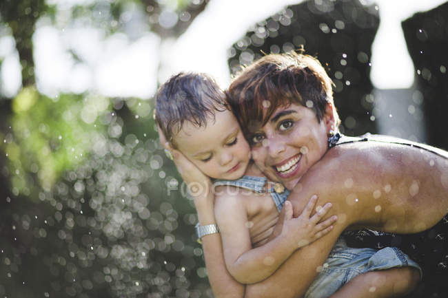 Joyeux petit garçon et mère profitant des éclaboussures d'eau dans le jardin — Photo de stock