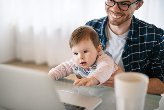 Portrait of baby girl sitting on father's lap looking at laptop — Stock Photo