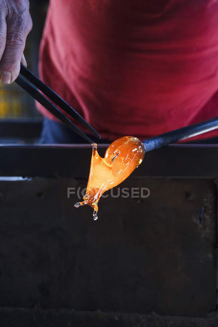 Человек, работающий с расплавленным стеклом с помощью пинцета на стекольной фабрике — стоковое фото
