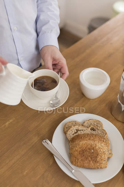 Людина заливки молоко в чашки кави на сніданок стіл, частковим видом — стокове фото
