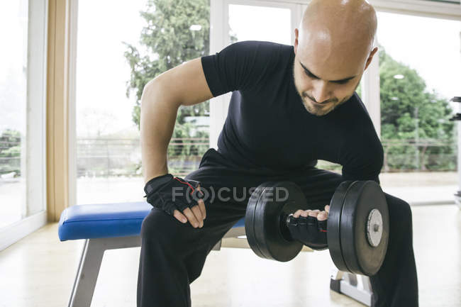 Man lifting a dumbbell sitting on a bench in a gym — Stock Photo