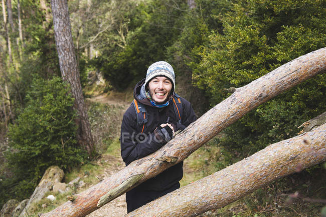 Felice giovane uomo appoggiato al tronco d'albero nella foresta — Foto stock