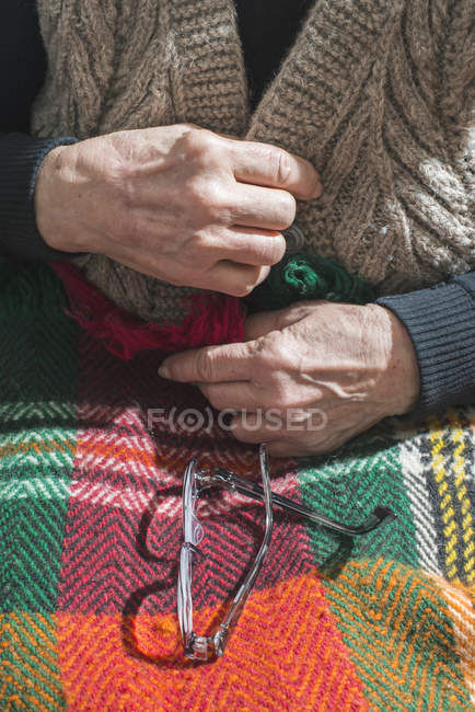 Руки пожилой женщины застегивают жилет, пока очки лежат на одеяле — стоковое фото