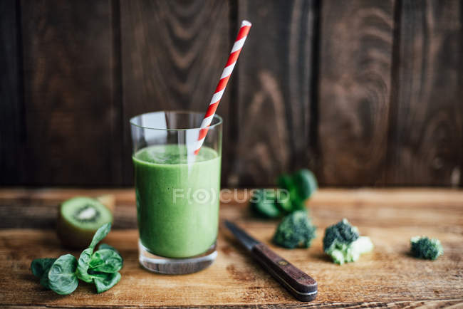 Vaso de batido verde con paja para beber en tabla de cortar - foto de stock