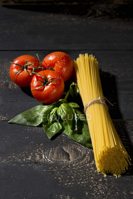 Spaghetti, basil and tomatoes on dark wood — Stock Photo