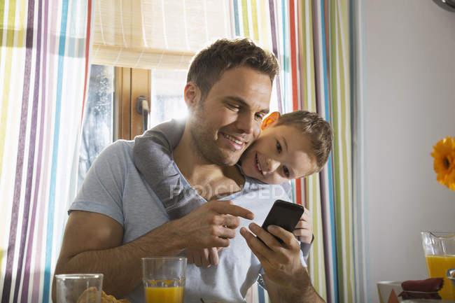Padre e figlio guardando smartphone al tavolo della cucina — Foto stock