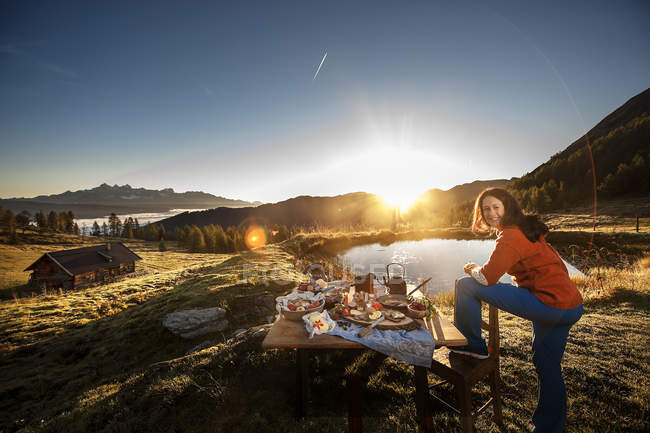 Austria, Stato di Salisburgo, Altenmarkt-Zauchensee, donna in piedi accanto al tavolo della colazione all'alba — Foto stock