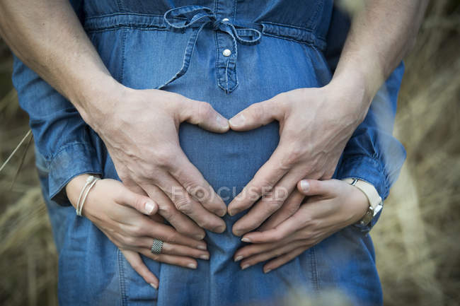 Рукою людини, утворюючи серце живота його вагітна дівчина — стокове фото