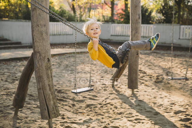 Boy having fun on a swing in playground and looking at camera — Stock Photo