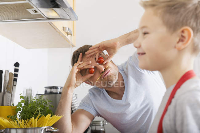 Батько покласти помідори як очі веселяться на кухні з сином — стокове фото