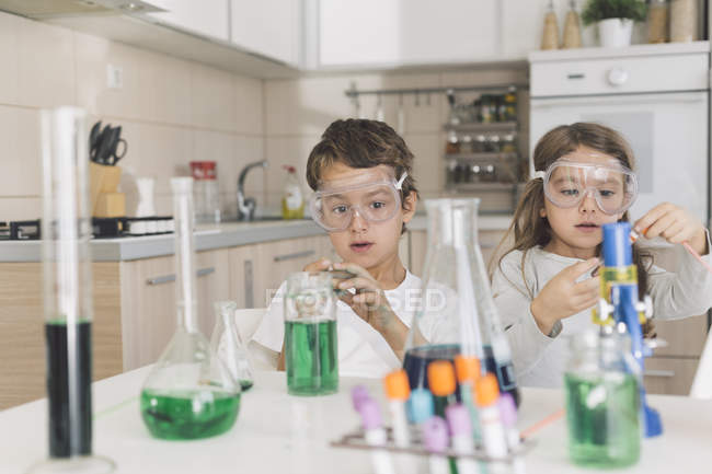 Niño y niña jugando experimentos científicos en casa - foto de stock