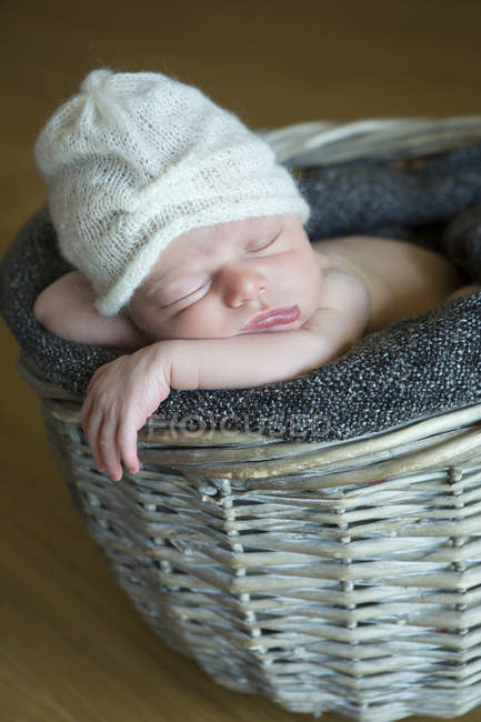 Retrato del recién nacido dormido en una canasta de mimbre con sombrero de lana - foto de stock