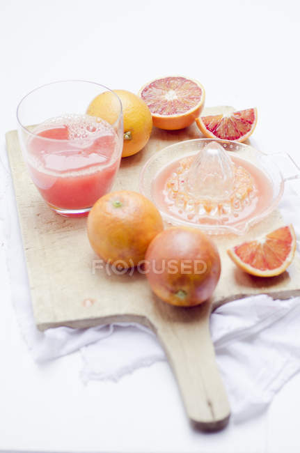Primer plano de vidrio con zumo de naranja rojo recién exprimido y naranjas rojas sobre tabla de madera - foto de stock