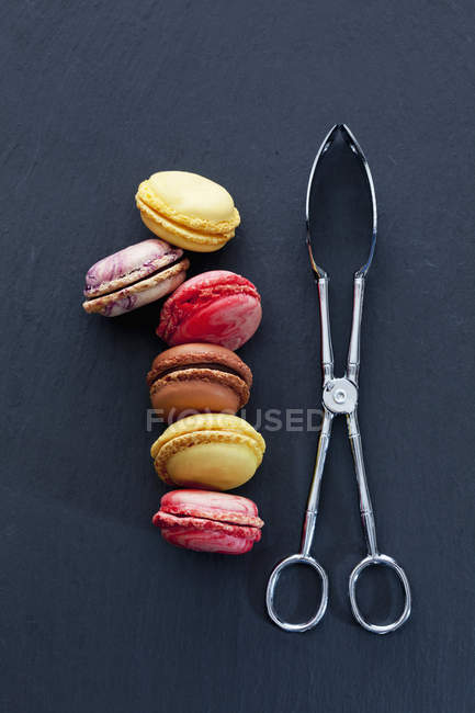 Шість різних macarons та тісто щипці на Шифер — стокове фото