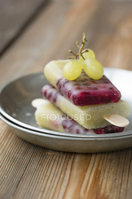 Dish with stack of selfmade grape pomegranate popsicles and green grapes — Stock Photo